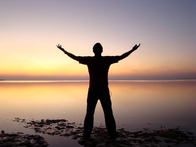 Silhouette d'un homme devant la mer, levant les bras vers le ciel